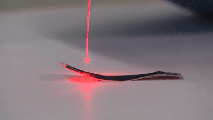 A laser beam hitting the curved surface of a metallic strip, producing a visible red dot and reflection near a pacemaker.