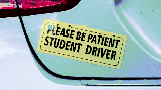 A car equipped with a sign that says "please be patient" indicating that it is driven by a student driver undergoing autonomous car training.