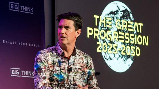 A man in a patterned shirt speaks on stage in front of a screen displaying "THE GREAT PROGRESSION 2025-2050" and the BIG THINK logo.