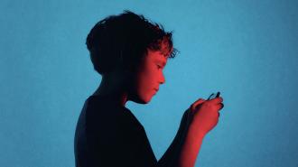 A young boy in profile looks down at a handheld device against a blue background, illuminated by red and blue lighting.