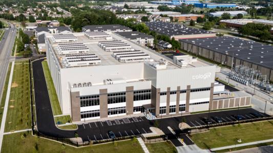 A large, modern industrial building with “Cologix” signage, surrounded by parking lots, roads, and green lawns in a suburban business area.