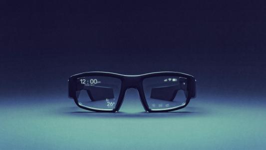 A pair of black smart glasses with a digital display showing the time, temperature, and icons on the lenses against a blue gradient background.