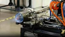 A close-up of an engine test firing, showcasing various connected hoses and cables, with the engine emitting blue flames from the nozzle, reminiscent of a powerful jet engine.