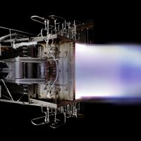 Rocket engine firing with a blue exhaust flame against a black background.