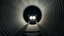 A train with bright headlights approaching through a large, dark, cylindrical tunnel.