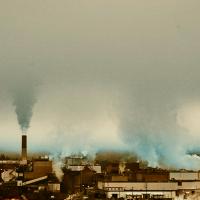 Industrial facility emitting smoke from multiple smokestacks under an overcast sky.