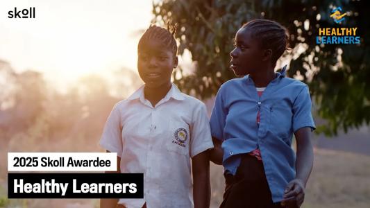 Two girls in school uniforms walk outdoors at sunset. Overlay text reads "2025 Skoll Awardee Healthy Learners" with Skoll and Healthy Learners logos visible.