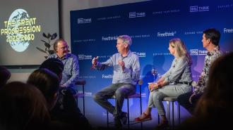 Four people sit on stage discussing "The Great Progression 2025-2050" at a panel event, with a screen and branded backdrop behind them.