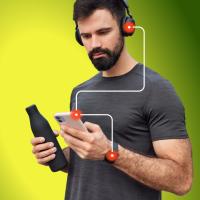 A man with headphones looks at his smartphone while holding a black water bottle, with a graphic overlay of connected points. The background is a gradient of green and yellow.