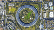 Aerial view of a large circular office building surrounded by trees, green spaces, and nearby roads in an urban area.
